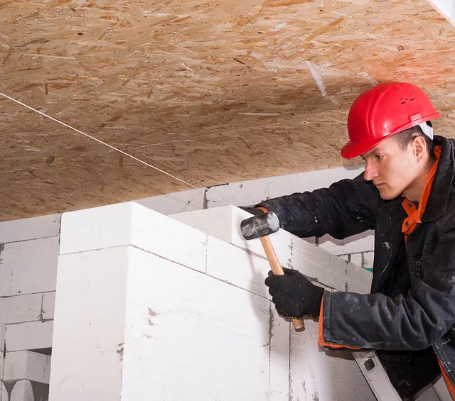En bild av en man med utrustning som placerar en tegelsten på en betongvägg